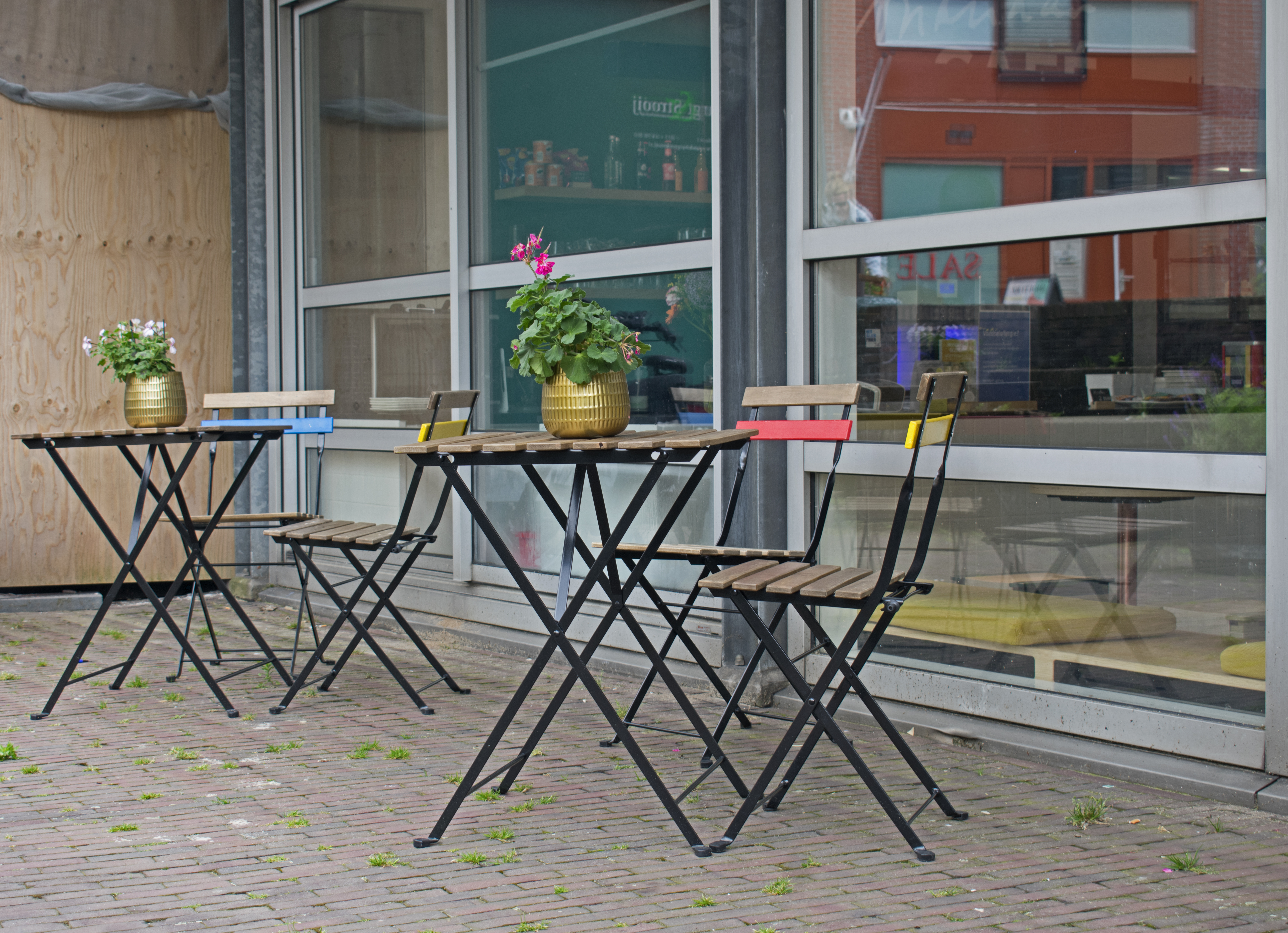 Two folding bistro tables with wooden slat chairs outside a glass shopfront