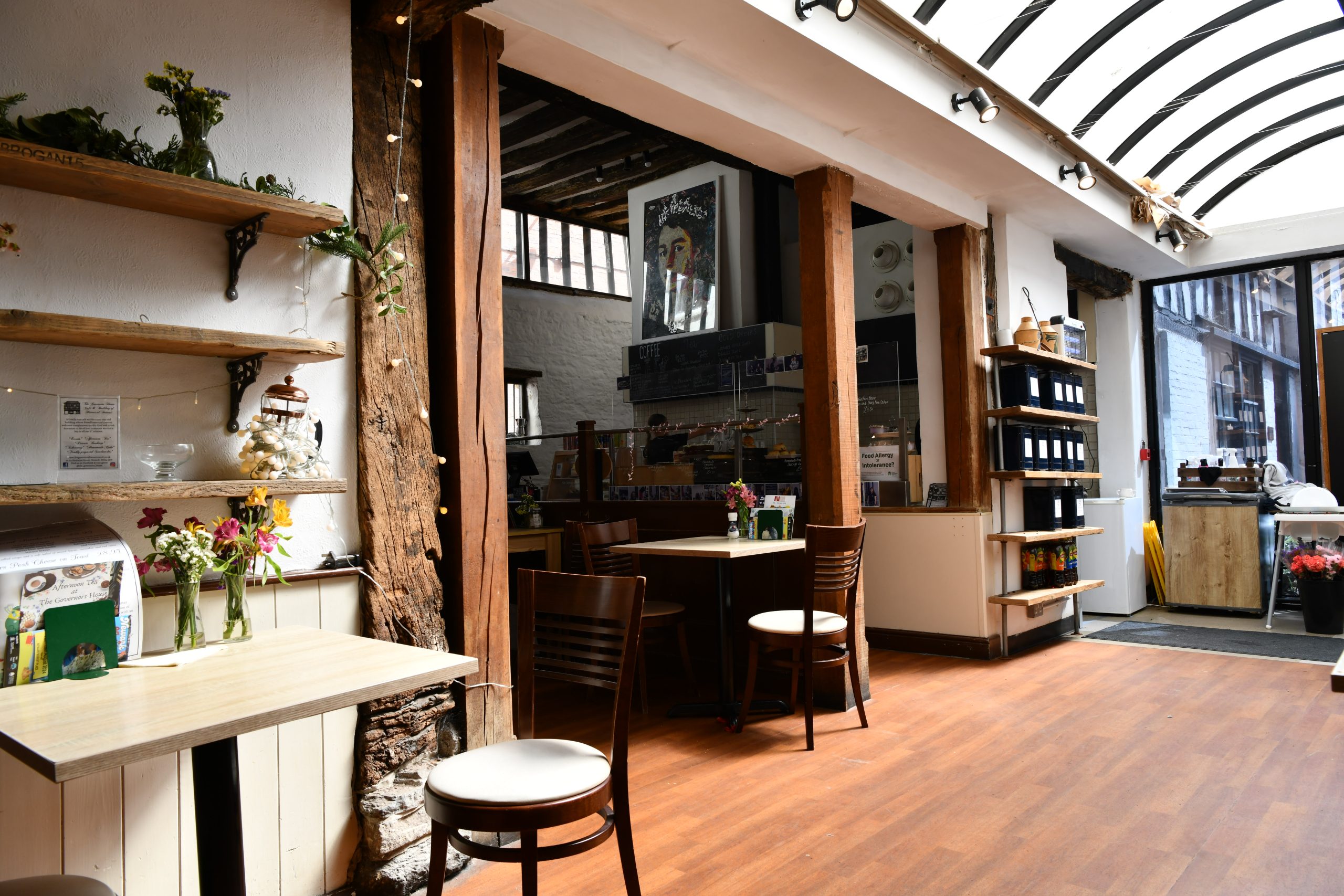 Small café interior with wooden tables, shelves of plants and a counter at the back