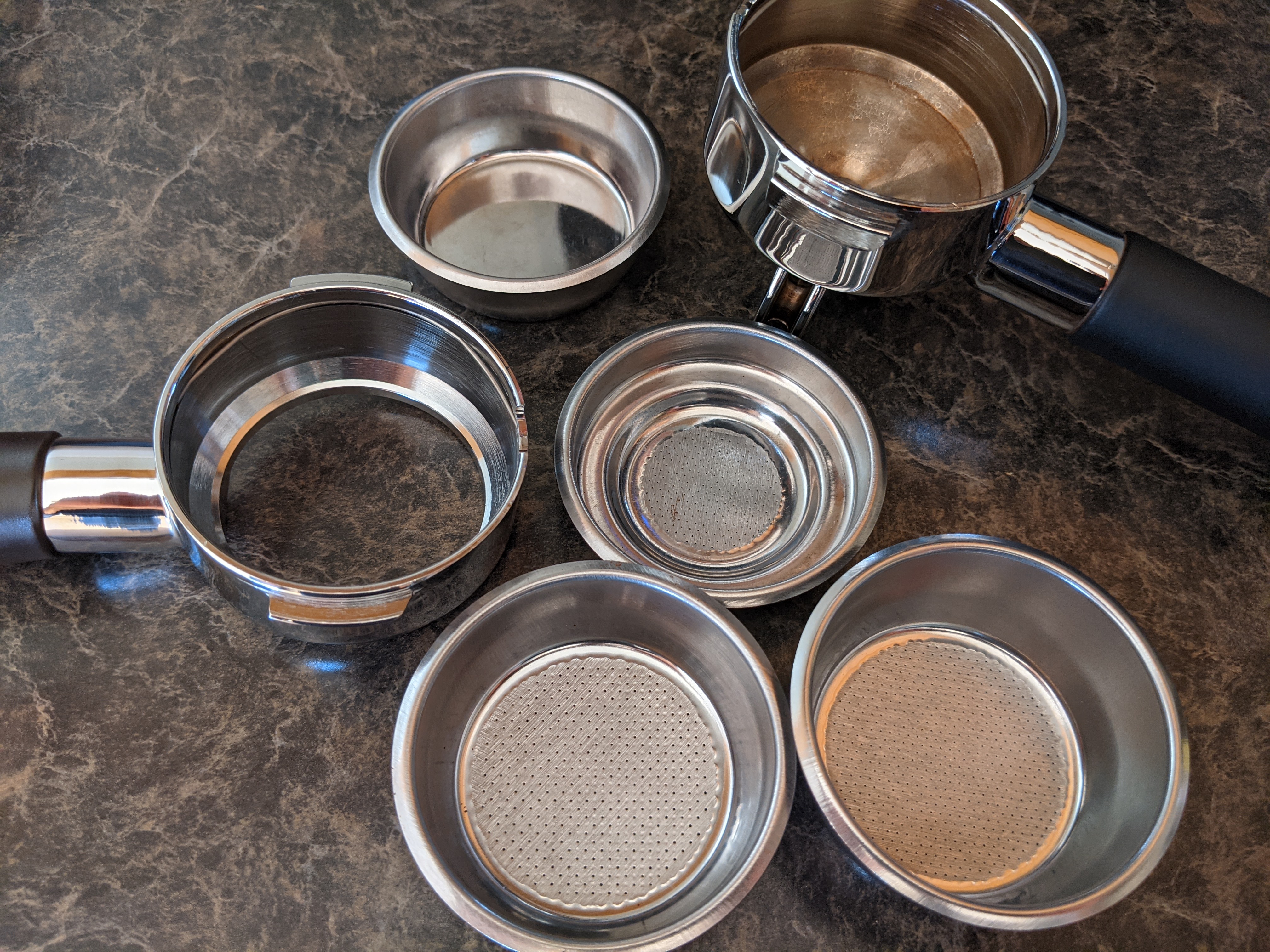 Two portafilters and several stainless steel filter baskets laid out on a countertop