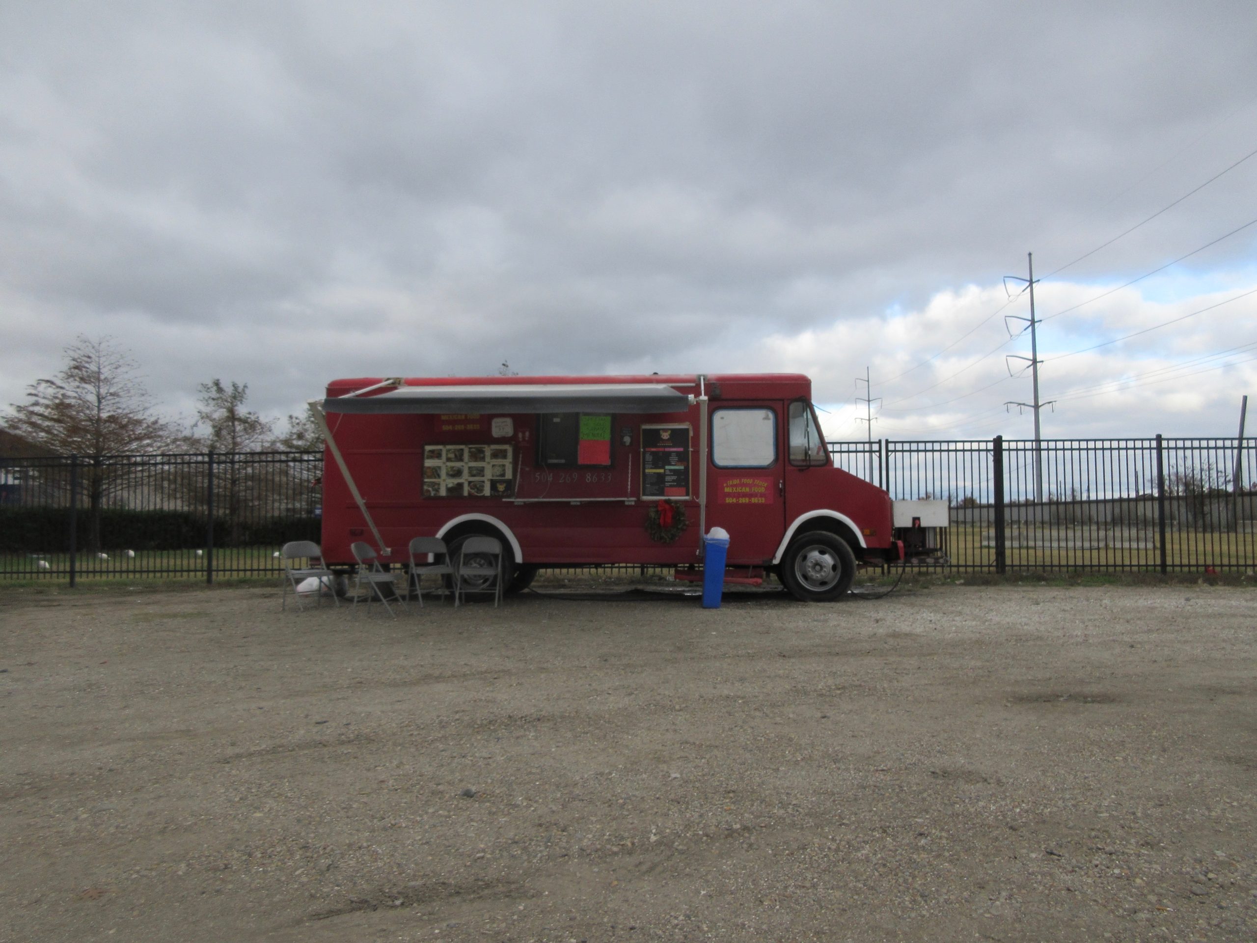 Red food truck parked on a gravel lot with folding chairs set out beside it