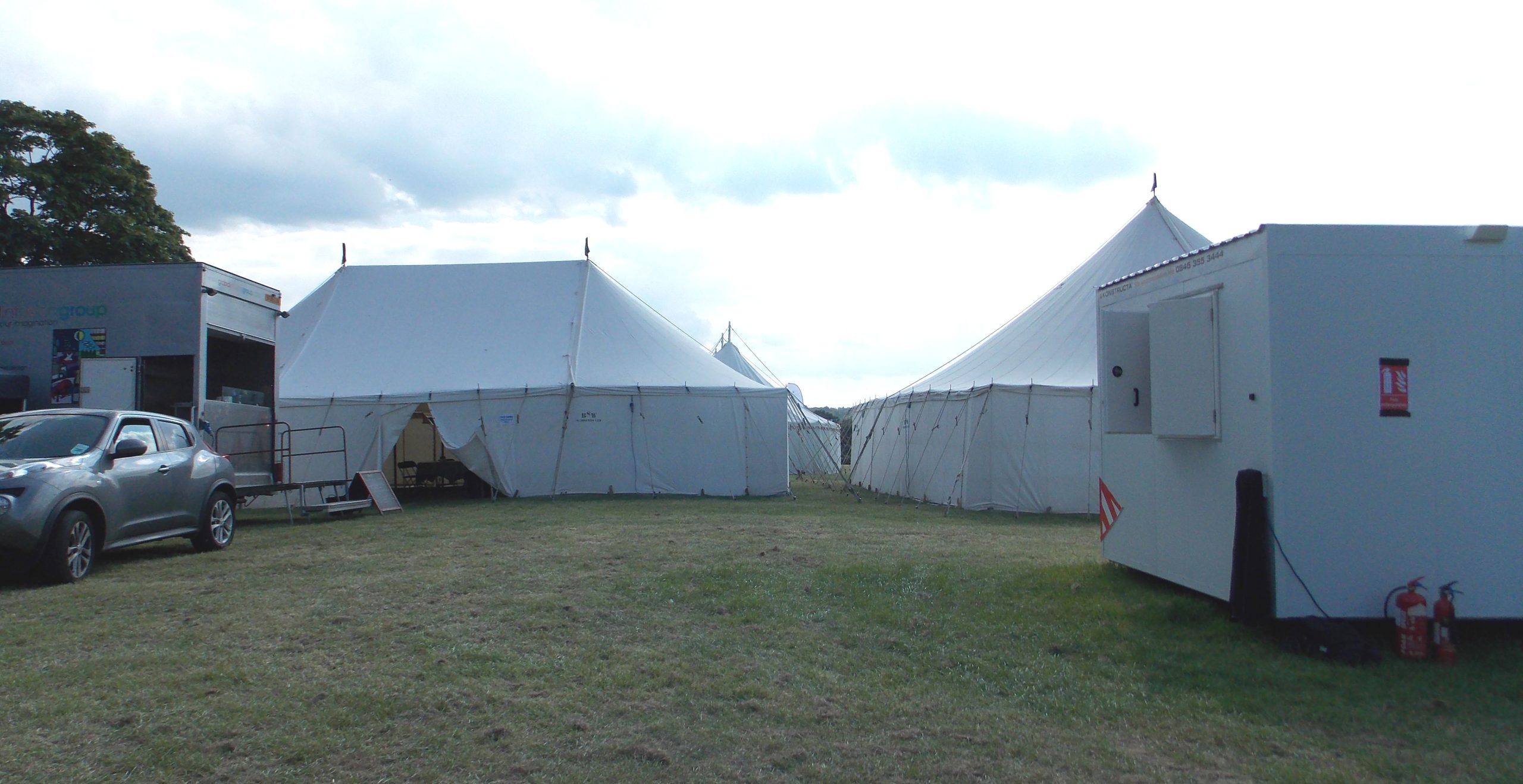 Event field with white marquee tents, a parked car and a portable catering unit on the grass