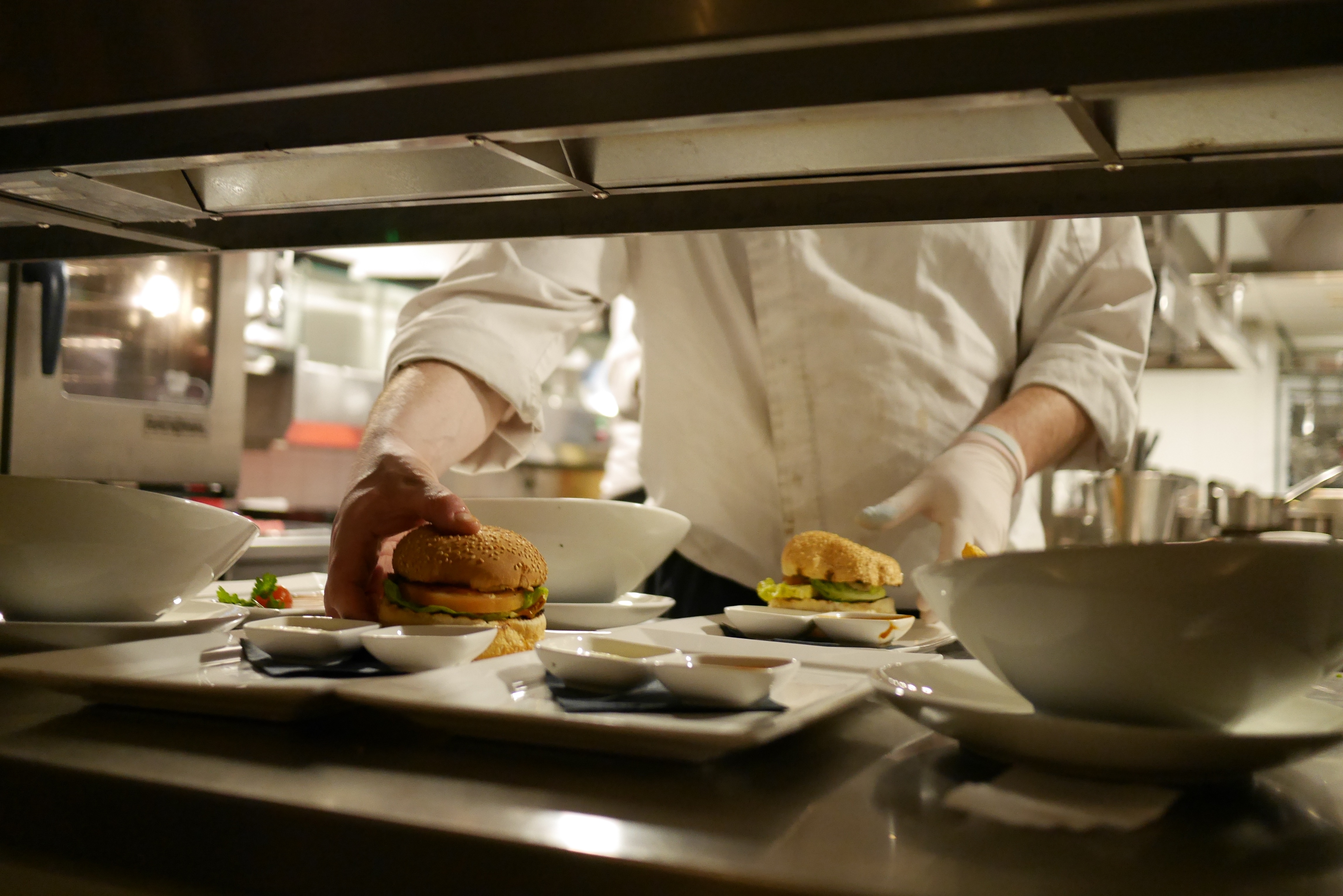Gloved cook plating burgers and small dishes at a restaurant kitchen pass