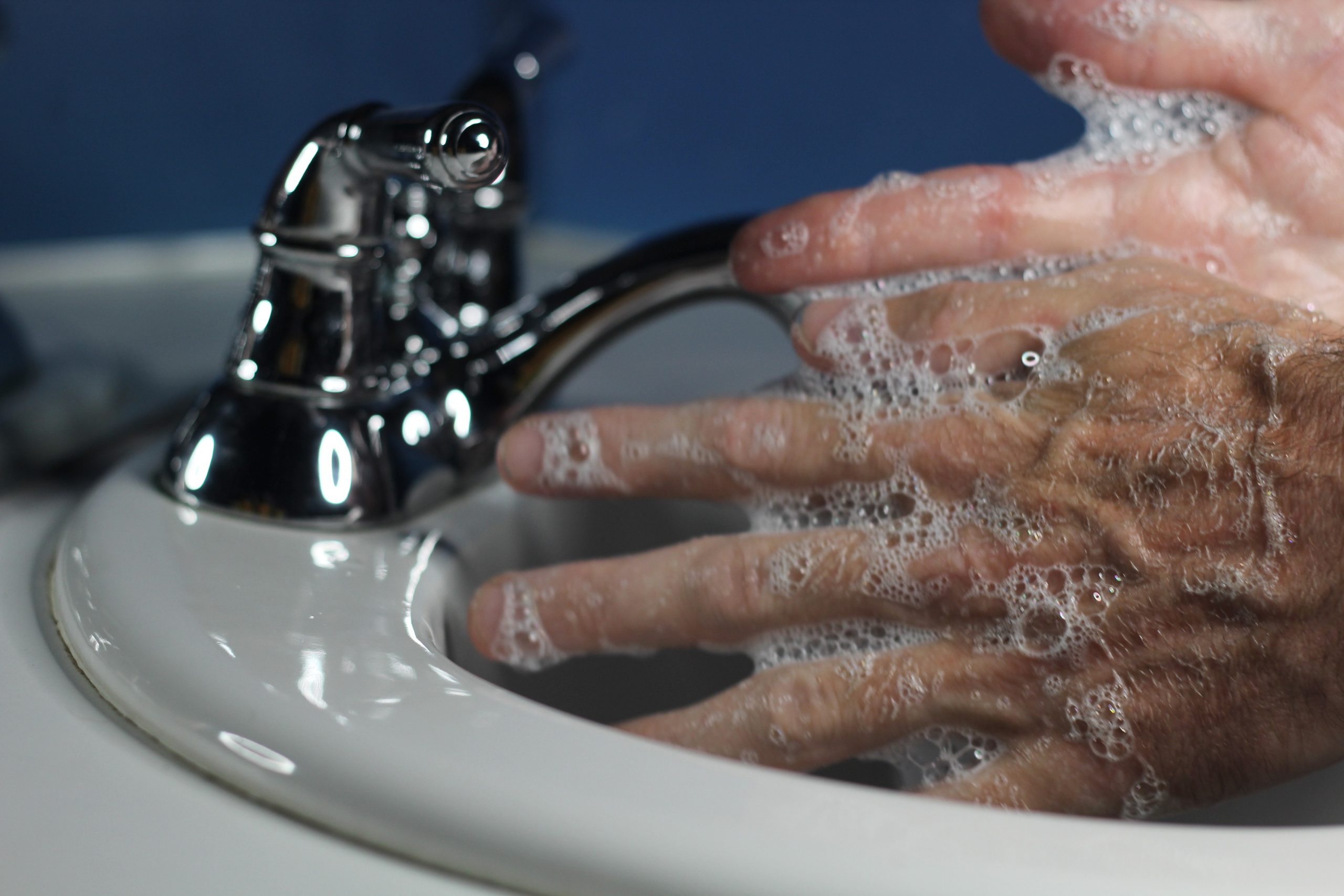 Soapy hands being washed under a chrome faucet at a white sink