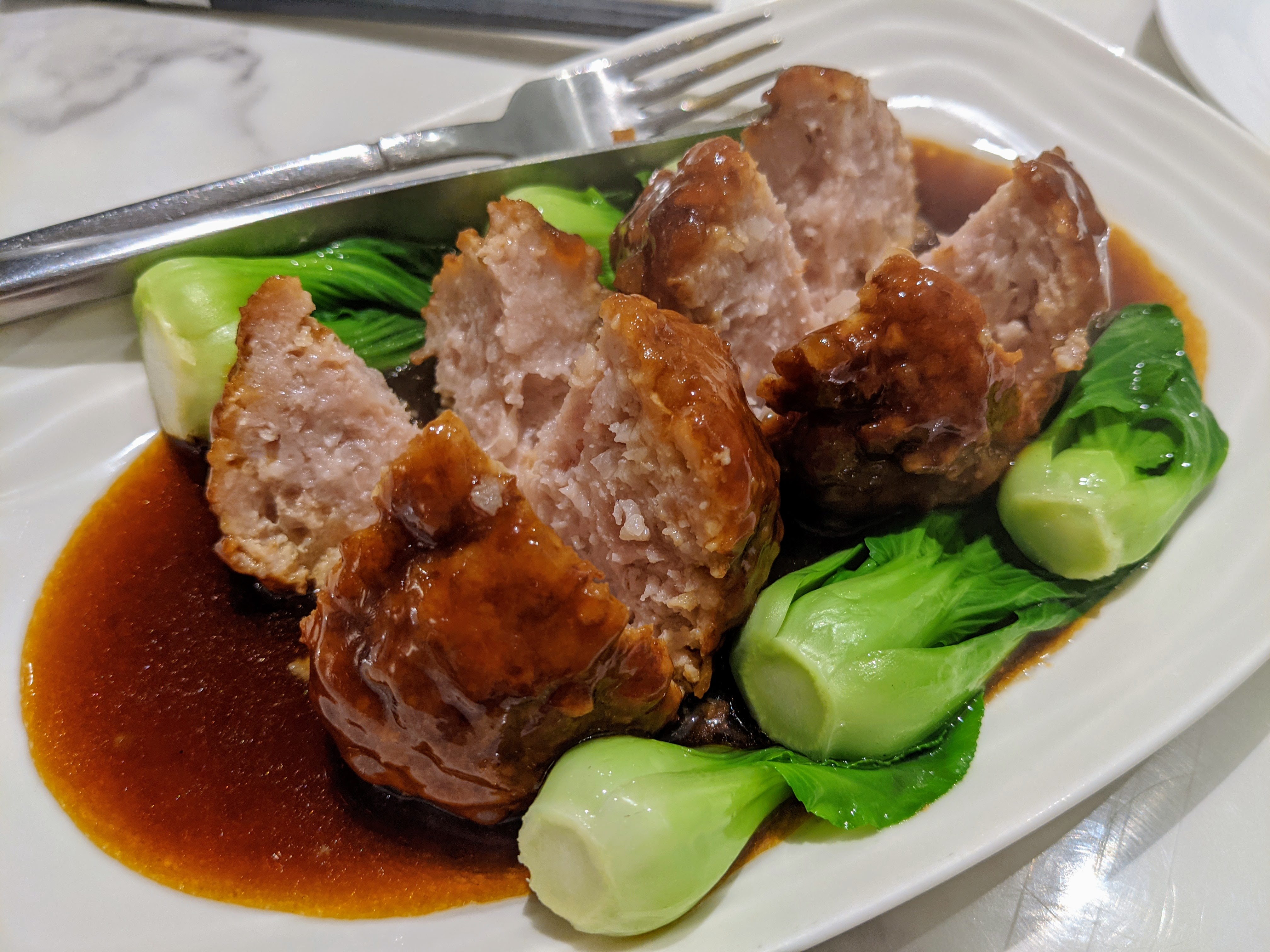 Plated meatballs in brown sauce with bok choy on a white plate