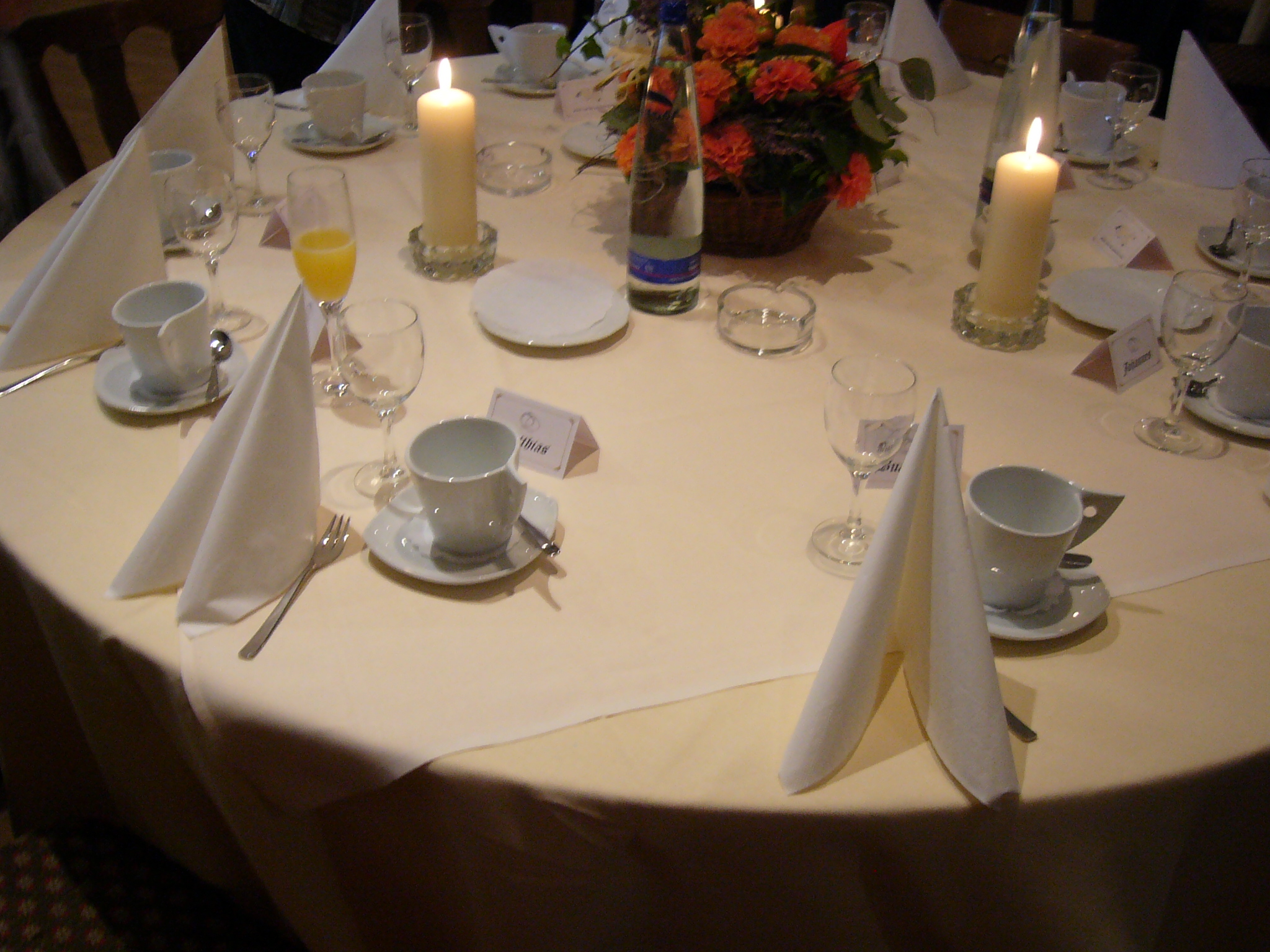 A round event table laid with folded napkins, cups, glasses, candles and a flower centrepiece
