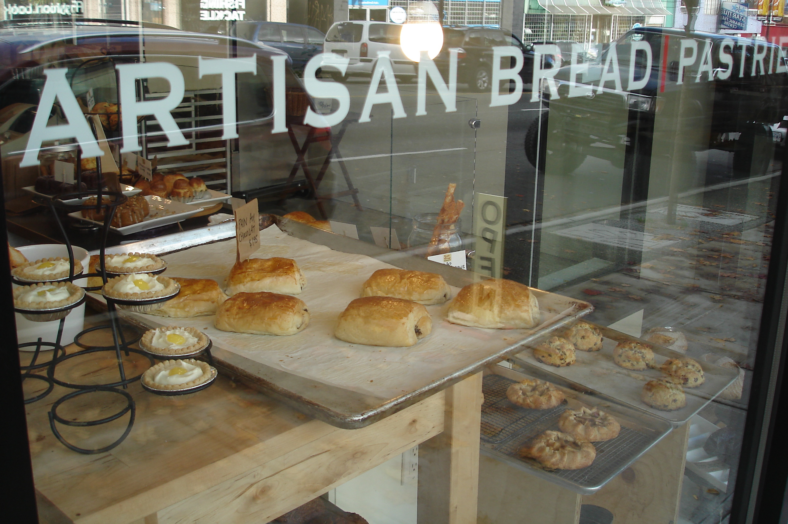 Pastries and tarts on trays behind a bakery window with lettering on the glass