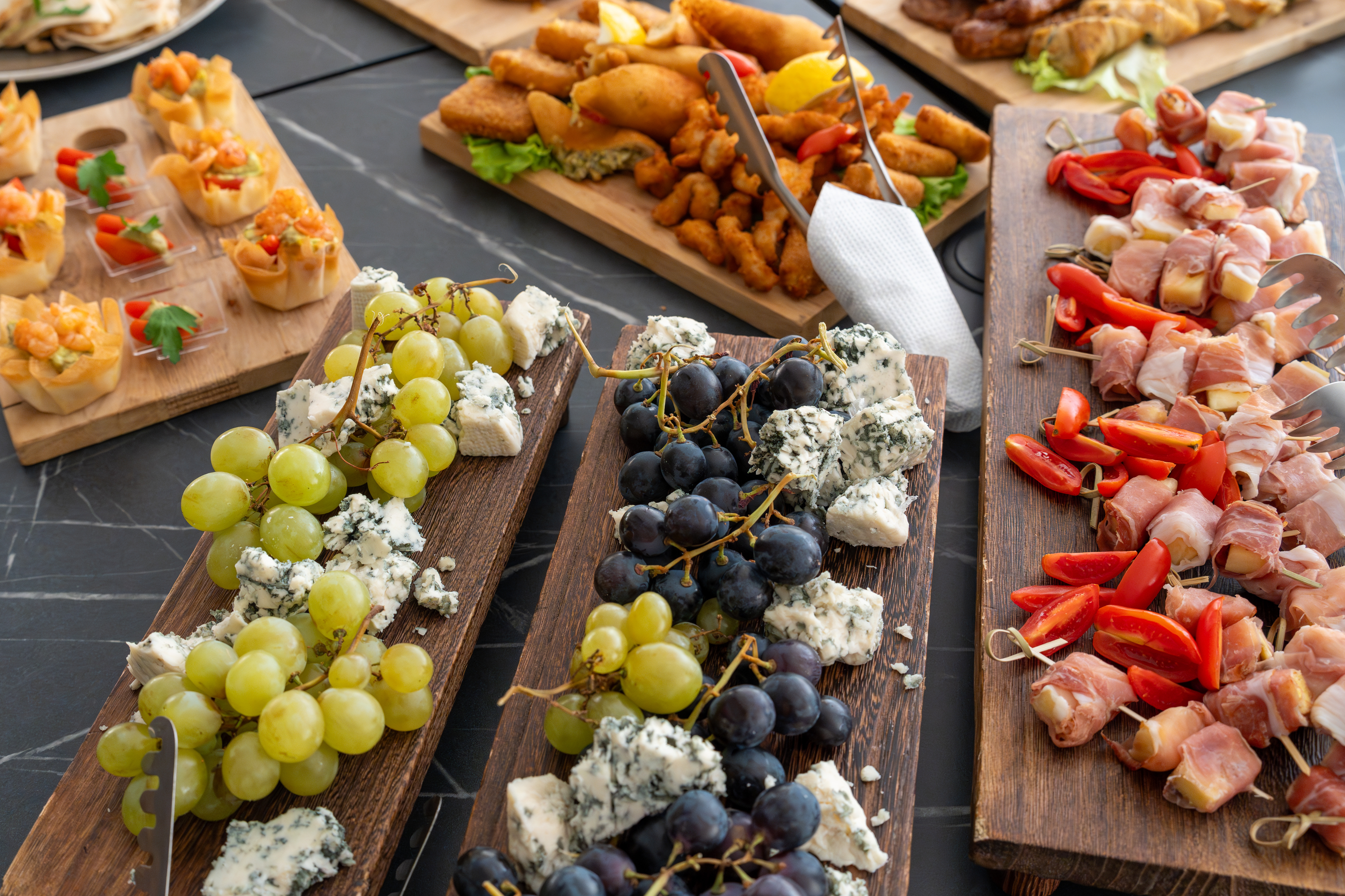 Wooden boards of finger food with grapes, cheese cubes and small skewers on a table