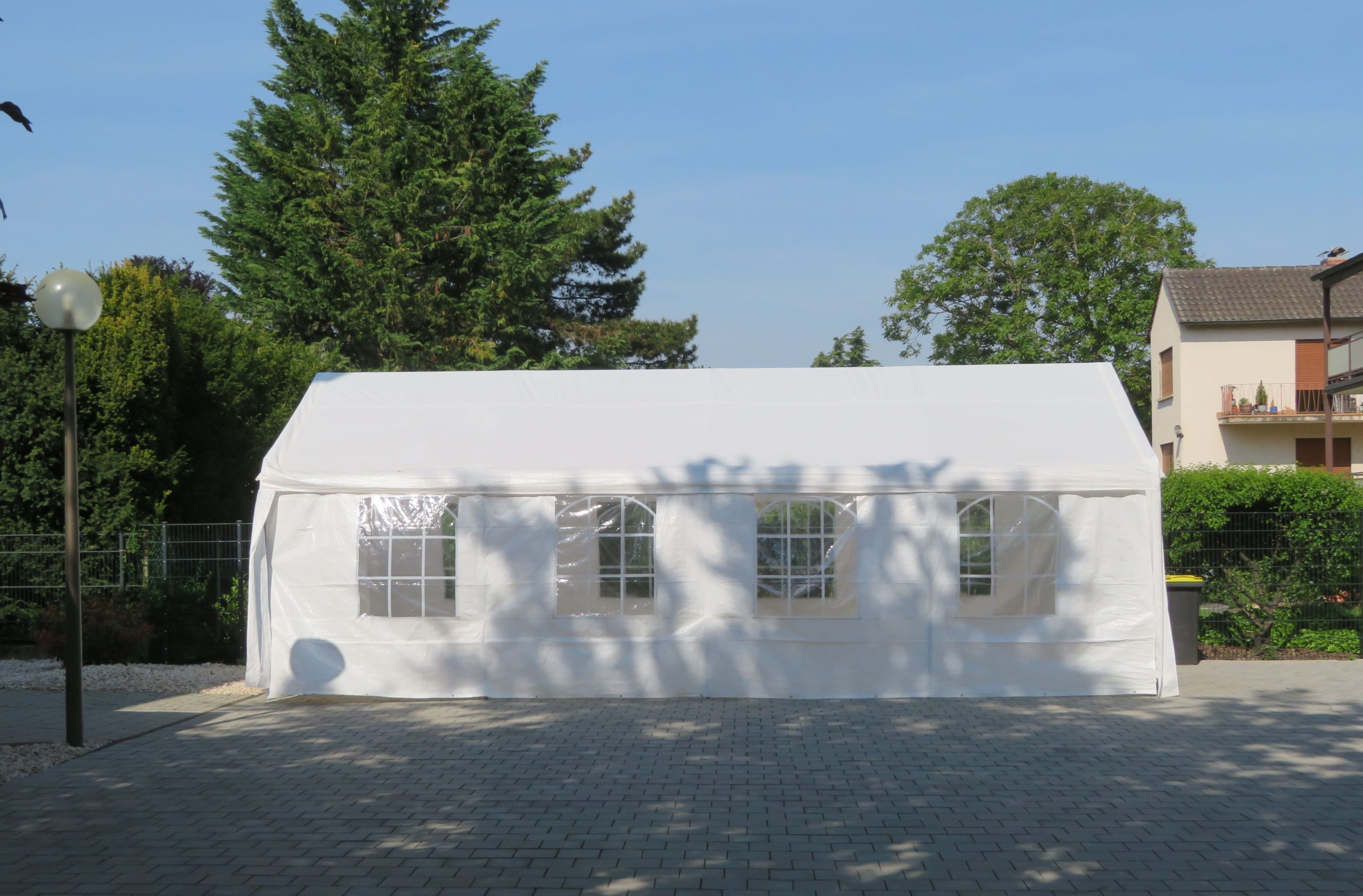 A white marquee with clear windows set up on a paved yard ready for an outdoor event