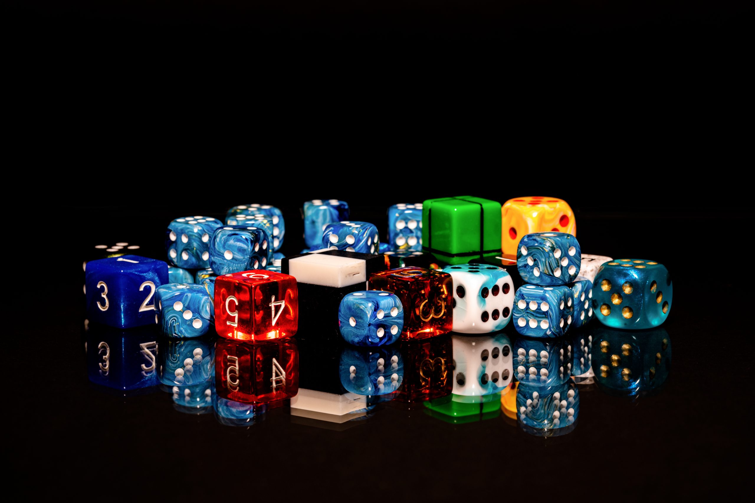 A pile of colorful six-sided and numbered dice on a glossy black surface