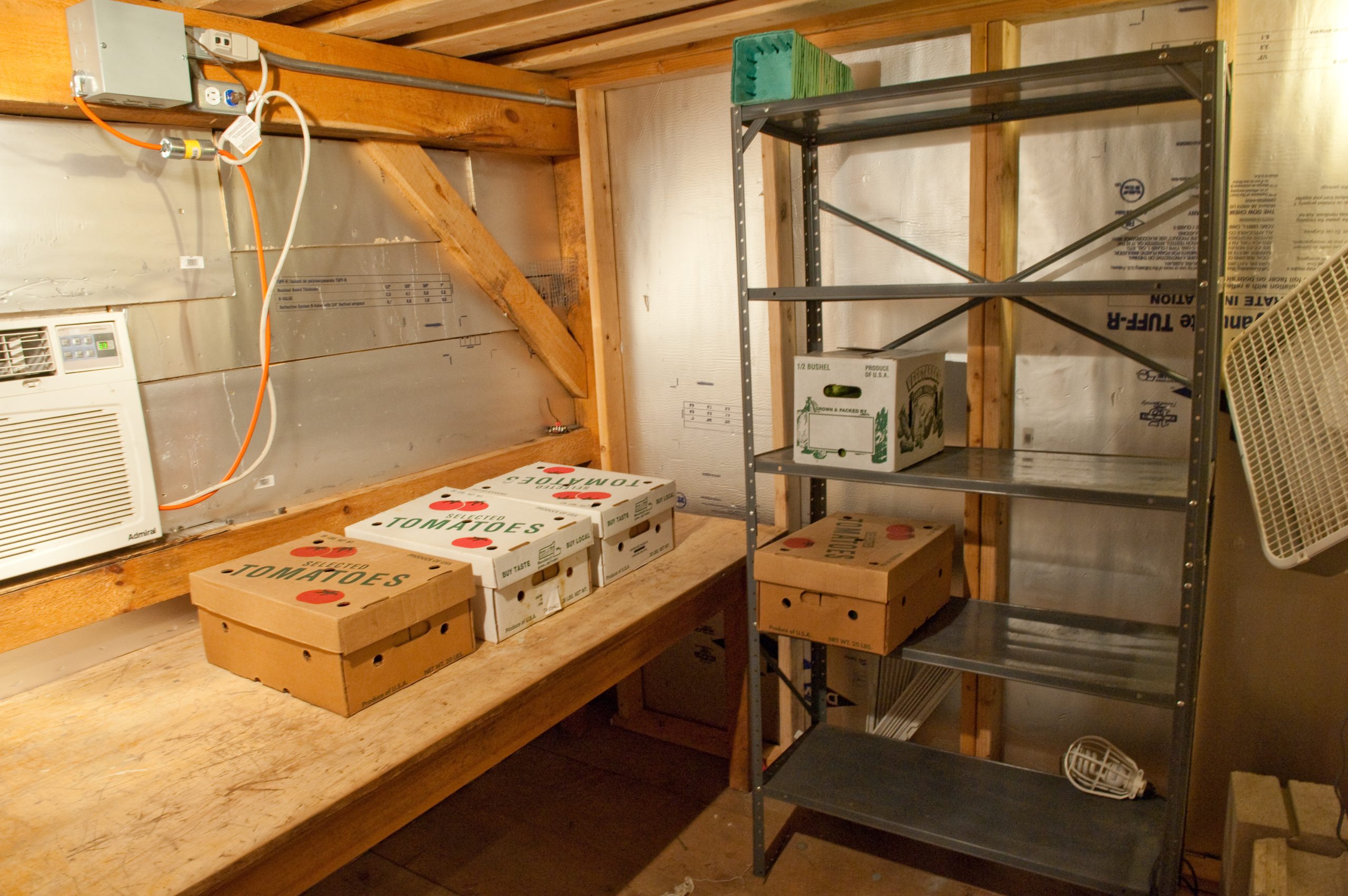 Cardboard produce boxes on a wooden bench and metal shelving inside a small walk-in cooler