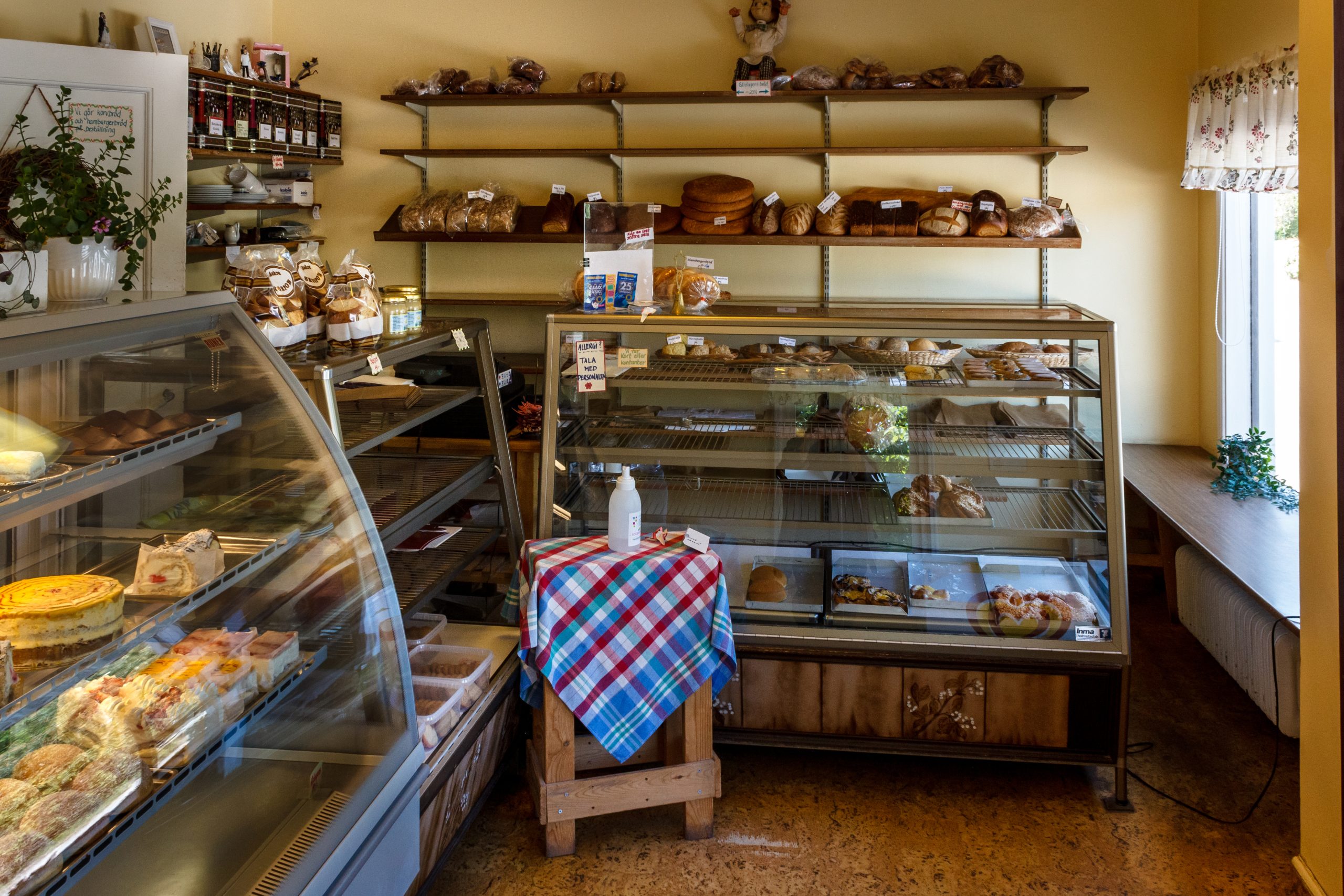 Glass display cases and wooden shelves of bread, cakes and pastries in a small bakery