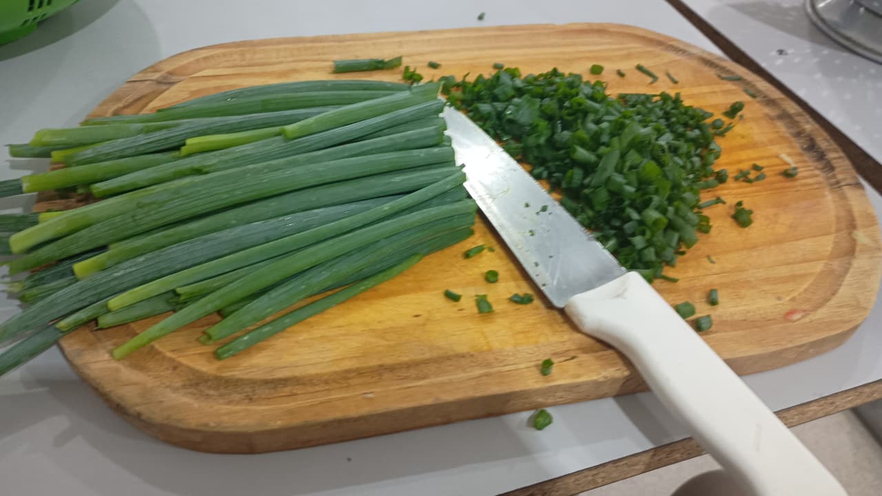 Green onions being sliced with a white-handled knife on a wooden cutting board