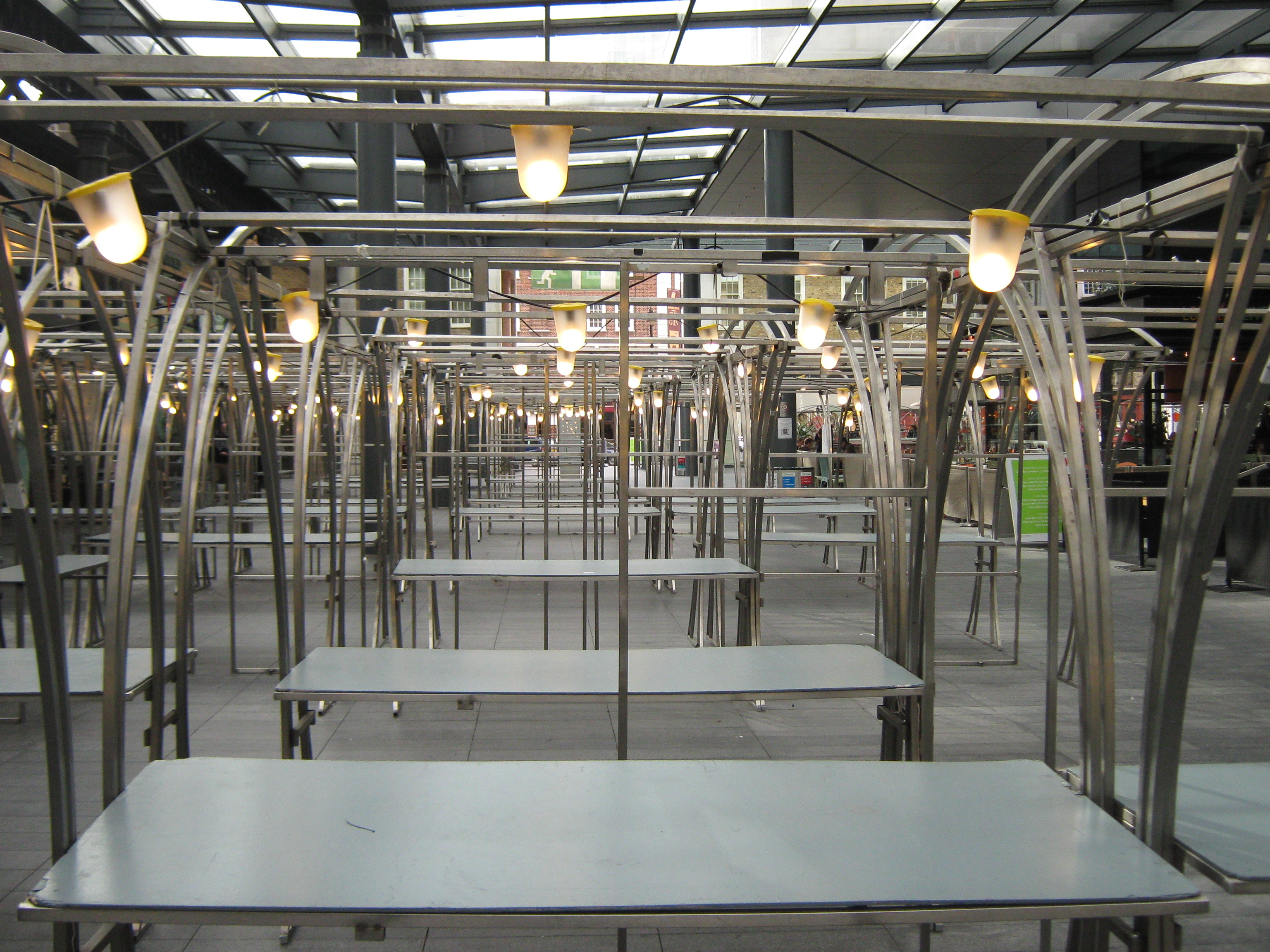 Rows of empty metal market stall tables with hanging lamps under a covered market roof