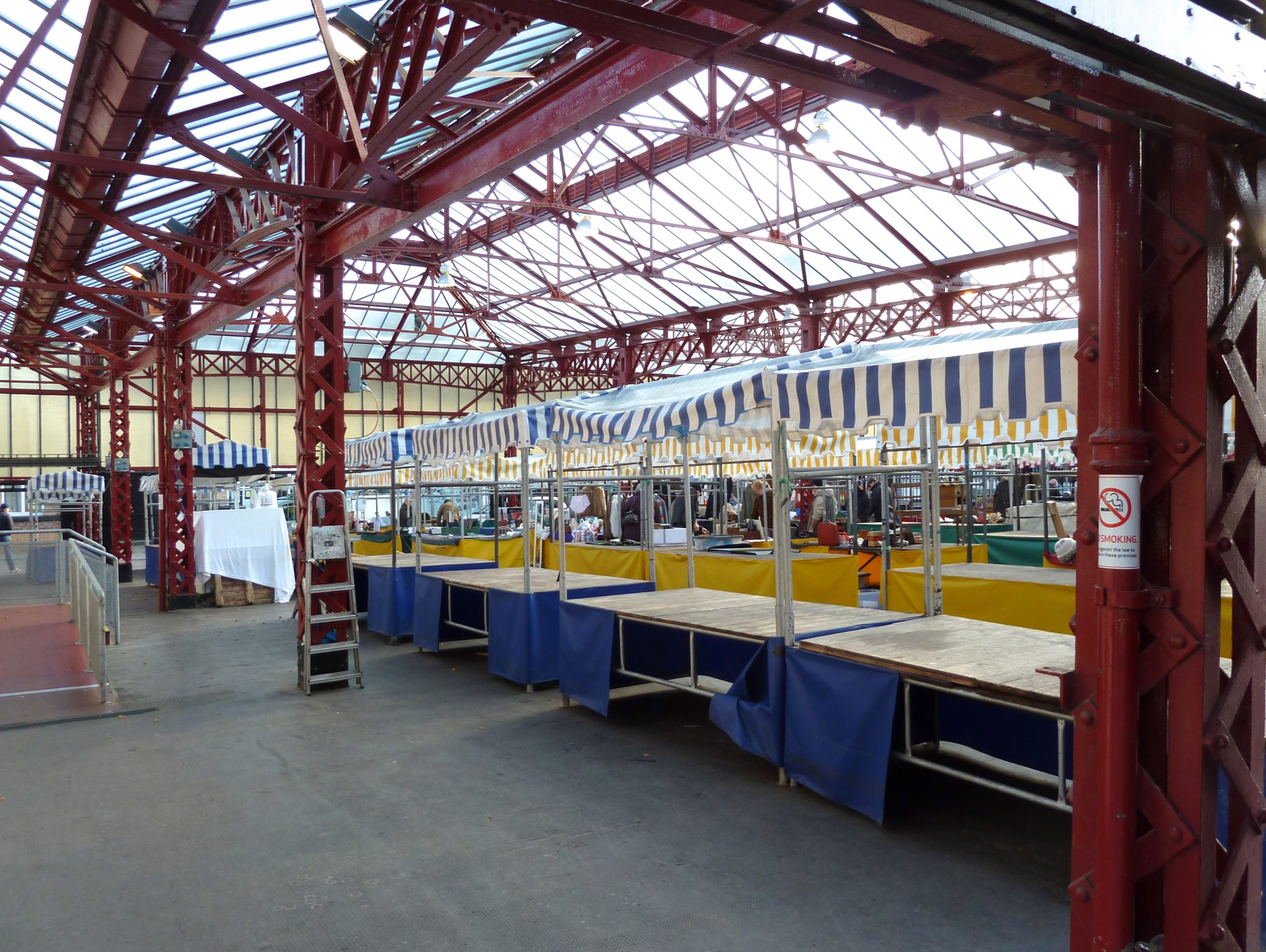 Rows of empty market stalls with striped canopies and boarded tops under a glass-roofed market hall