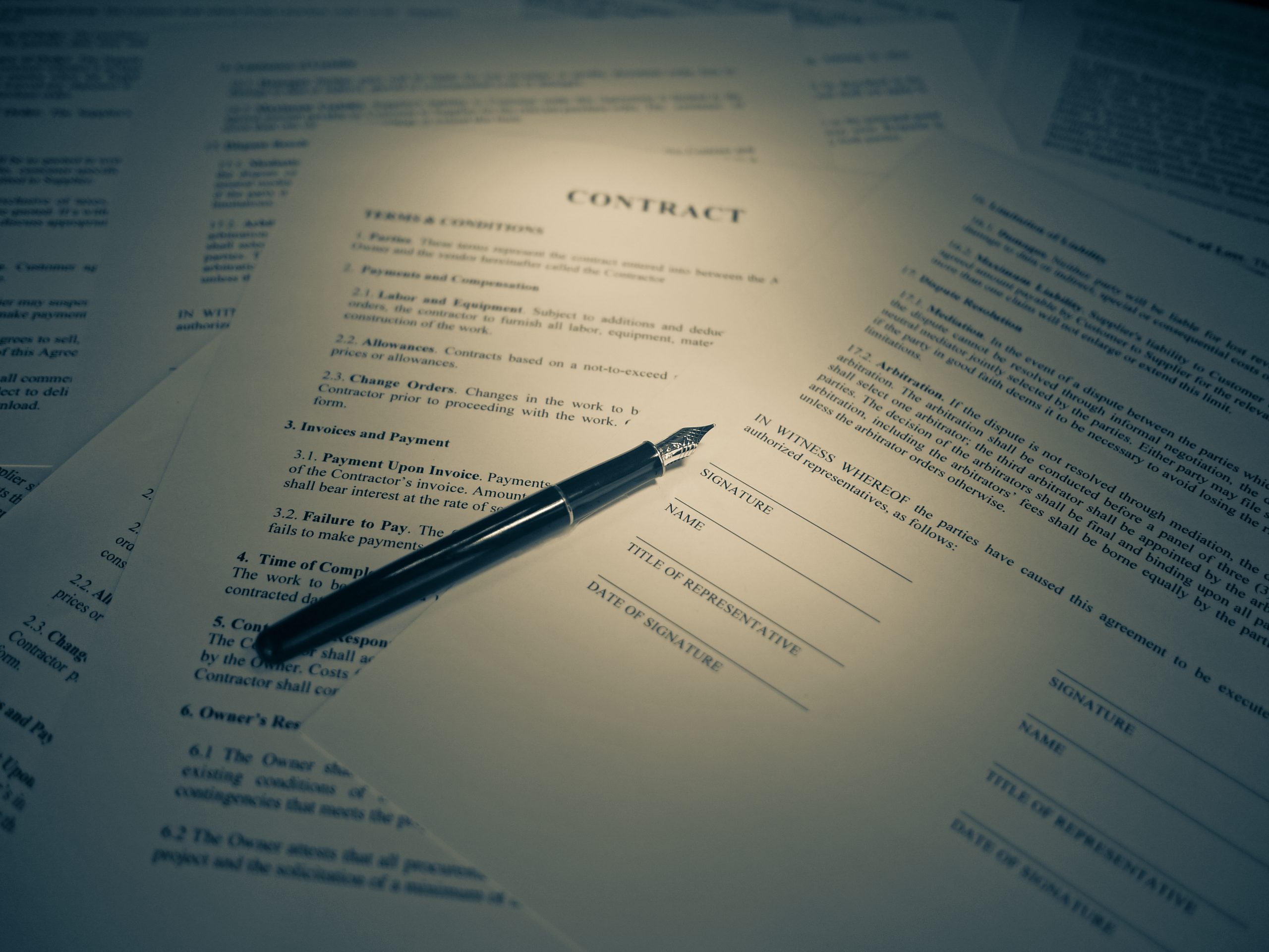 Printed contract pages spread on a desk with a fountain pen resting on the signature lines