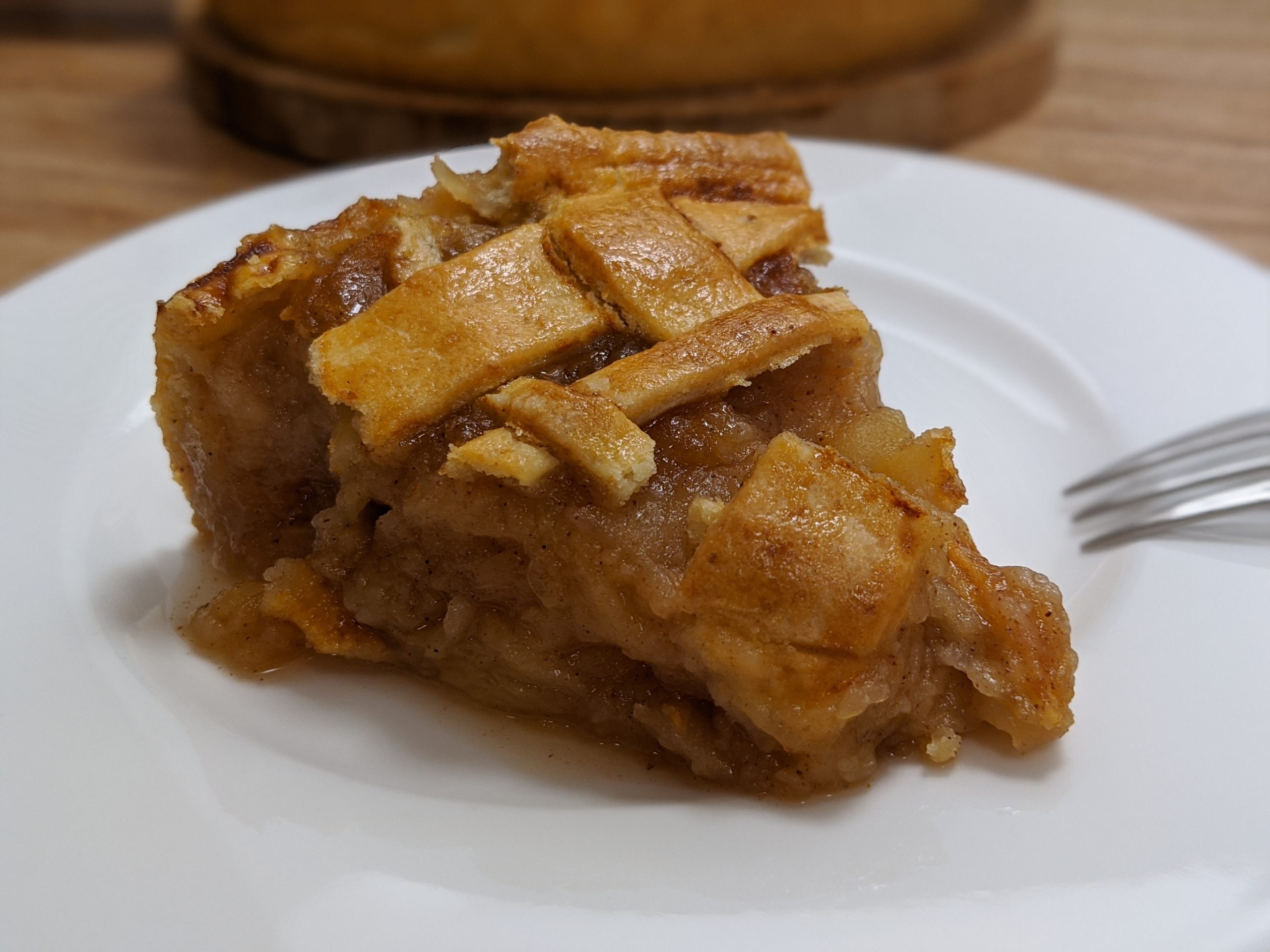 A slice of homemade lattice-topped apple pie on a white plate with a fork
