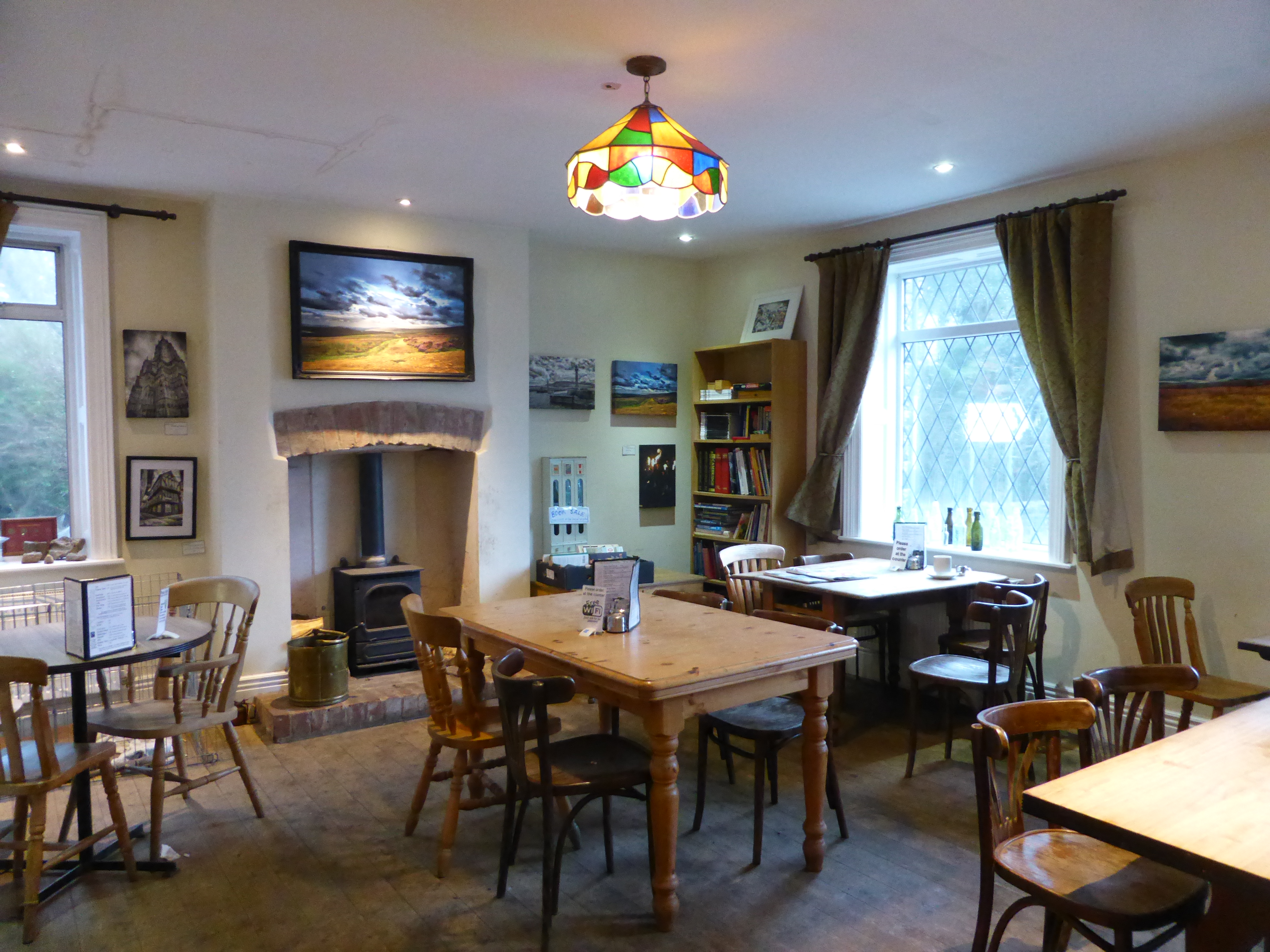 A quiet small cafe dining room with wooden tables, a wood stove and bookshelves