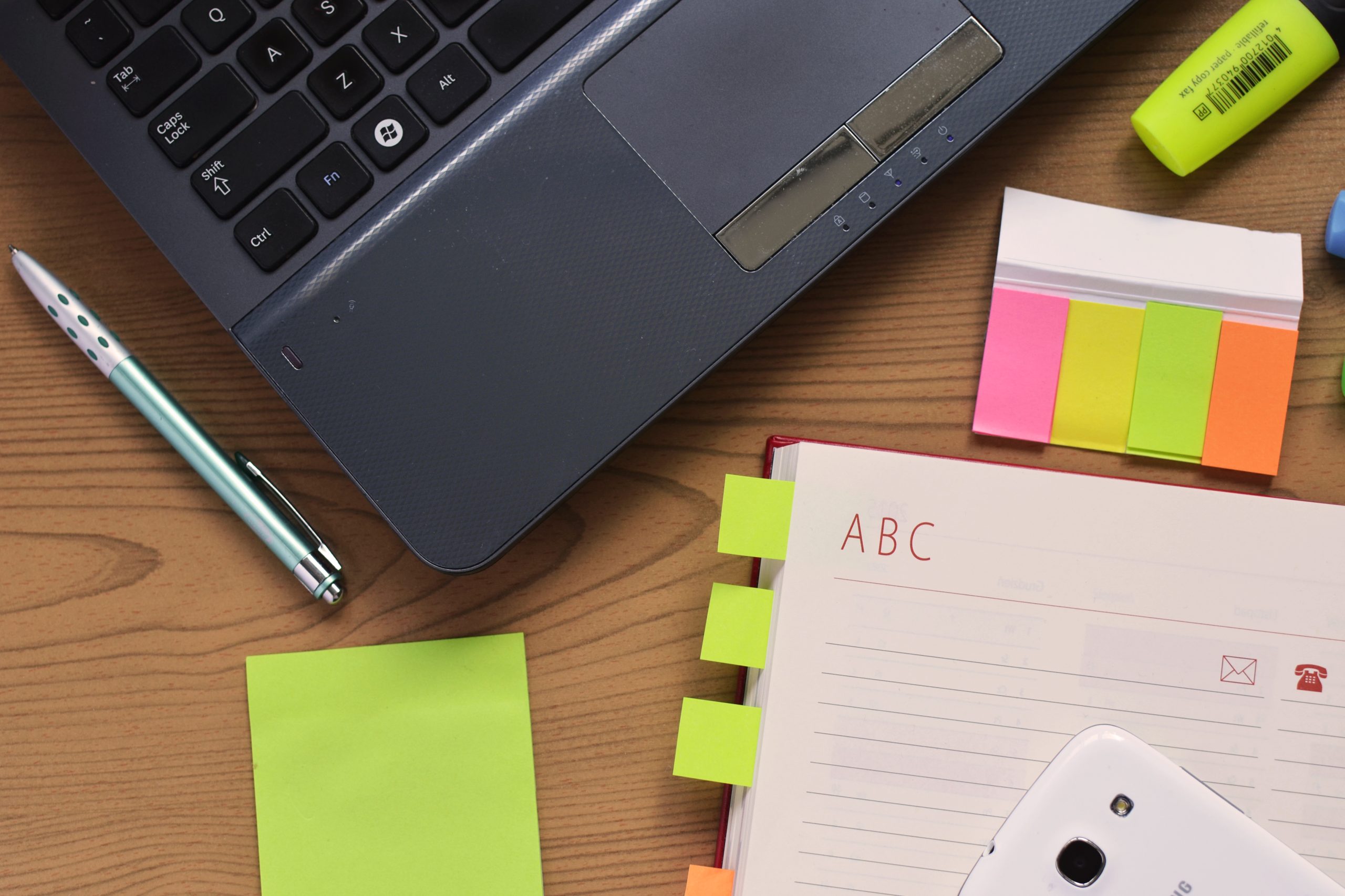 A laptop, an open notebook with sticky notes and a pen on a wooden desk