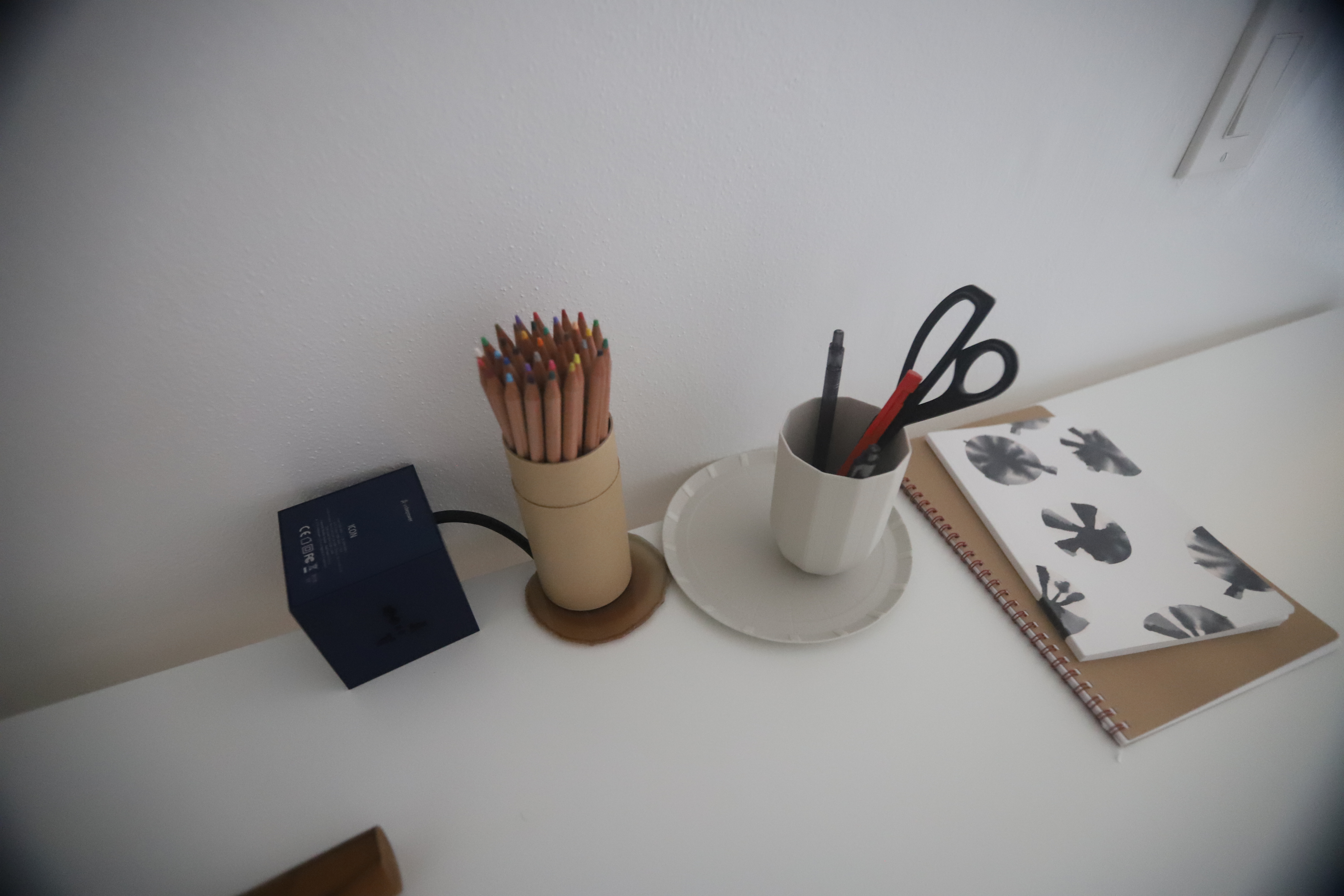 A tidy desk with colored pencils in a holder, a cup of pens and scissors and a notebook